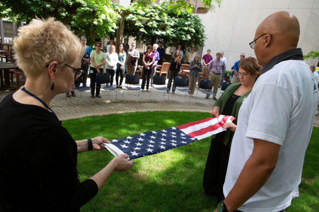 Thre people stand holding different sides of an American flag while other people look on solemnly.