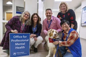 Four people with an Office of Professional Mental Health sign crouch behind a dog named Rocky and his handler.